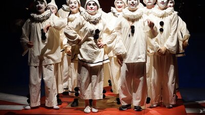 group of 12 young people dressed as clowns in all white with black pompoms and white make-up