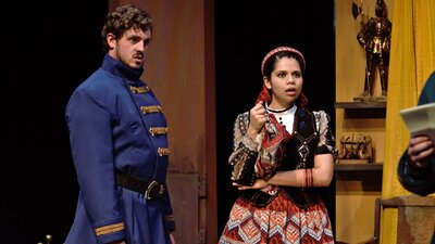 a young man in blue army coat and young girl in traditional Spanish dress look shocked