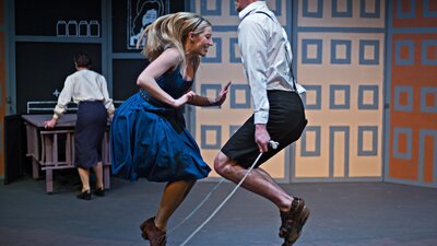 a young blond female wears a blue dress and jumps rope with a young man in white shirt and breeches