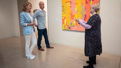 A gallery curator and couple standing in front of an artwork