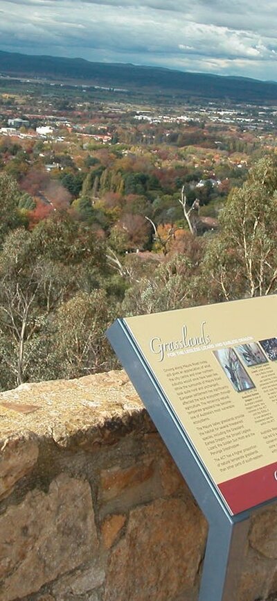 Sign leaning against stone wall with view of trees and distant houses