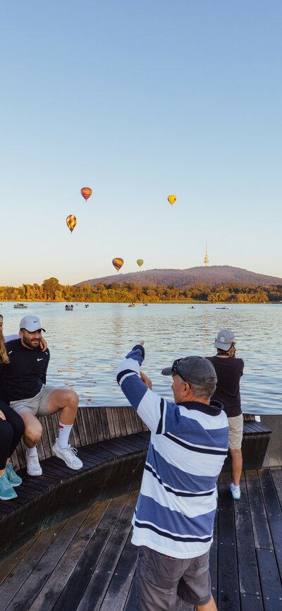 People taking photos in front of hot air balloons by the lake