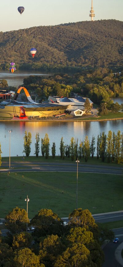 Aerial view of National Museum of Australia with hot air balloons and Black Mountain in the background. 