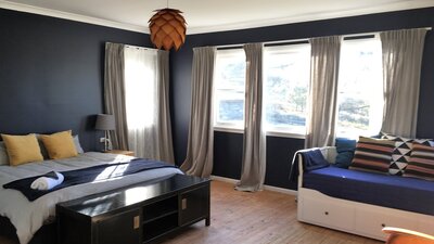 Big sunny bedroom with dark blue walls & light timber floor. King bed & daybed, colourful cushions.