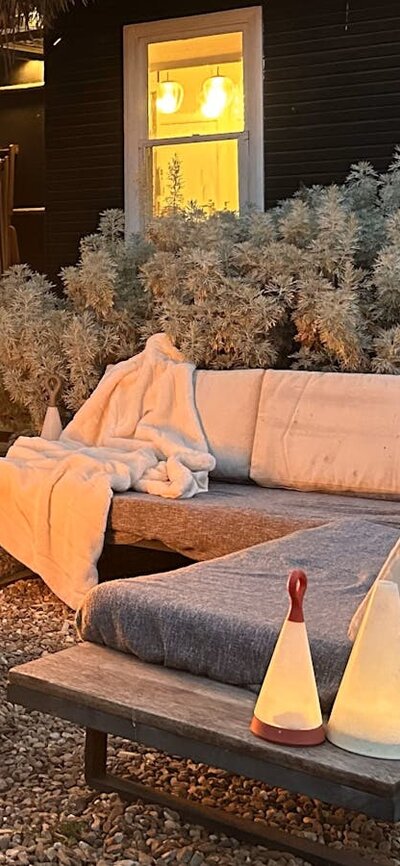 Firepit at dusk with outdoor couch, house in the background with lights on.