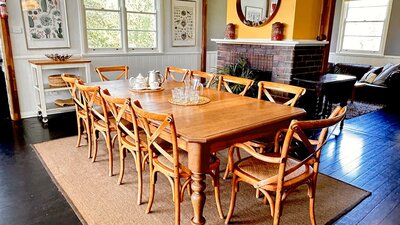 Large dining table on rug with fireplace behind, art, mirror, daylight in windows