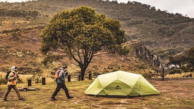 Two men walk past a green tent at Blue Waterholes campground, Kosciuszko National Park. Photo: