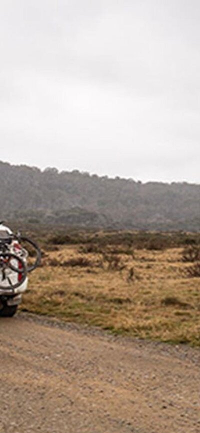 A car carrying bikes drives past a sign on an unsealed road, Kosciuszko National Park. Photo: Robert