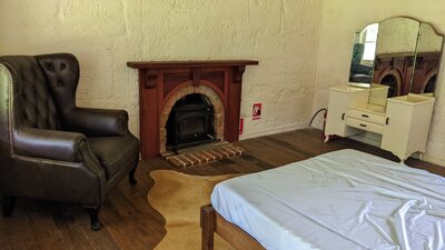 Bedroom with double bed, fireplace, wingback chair and vintage dressing table with mirrors