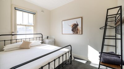 Room with king bed and sink beside it. Photo of a bull on wall as well as clothing rack.