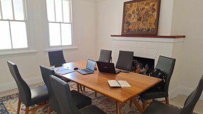 Meeting Room with board table and eight chairs. Laptops and paperwork on table. Painting on mantle.