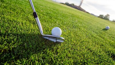 Golf club lining up shot on golf ball on green grass