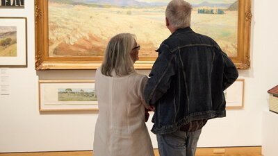 Visitors observing a landscape painting in the Canberra/Kamberri exhibition