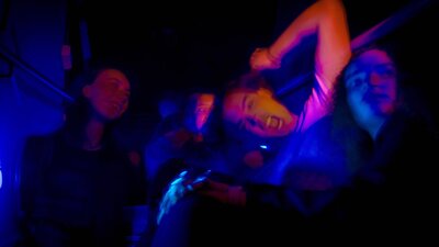 A group of teenagers sit around on a staircase in intense nightclub light.