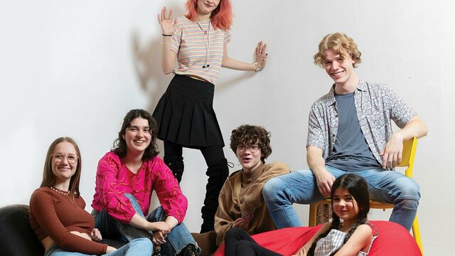 Canberra Youth Theatre is a space for young people to belong. A group of six smiling young people aged 12–18 sit on bean-bags and chairs, facing the viewer.