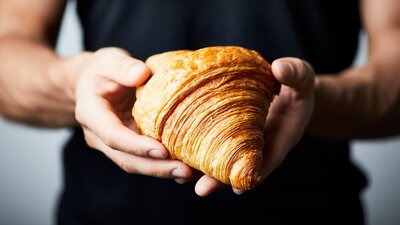 Person wearing black shirt holding a golden croissant