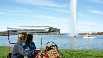 Couple cycling past Captain Cook Memorial Jet in Canberra