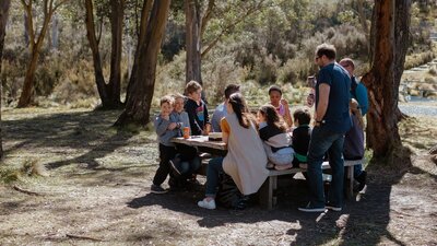 Three families enjoying lunch around a picnic table amongst gum trees.