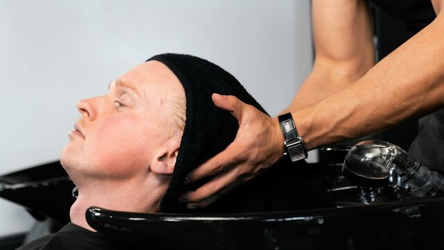 A client relaxing in a barber wash station while receiving a scalp treatment and head massage