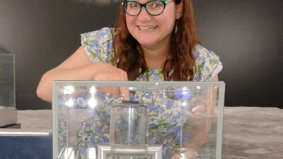 A woman touches a small rock  in a cabinet with an image of the Moon and Earth behind her.