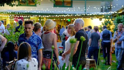 People milling in the Gorman Courtyards at twilight, surrounded by leafy foliage and fairylights