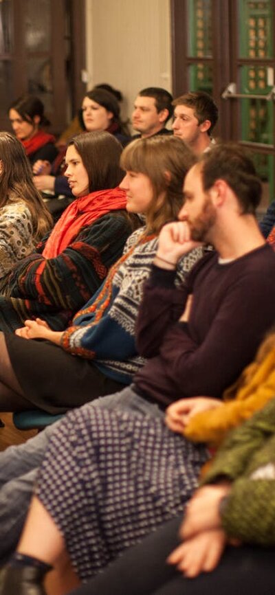 A crowd of seated people watching a poetry performance (performer outside of the frame)