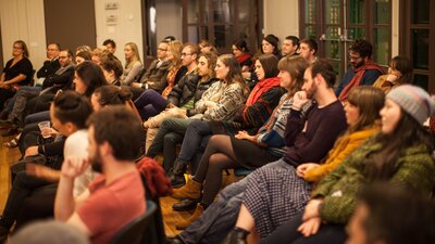 A crowd of seated people watching a poetry performance (performer outside of the frame)