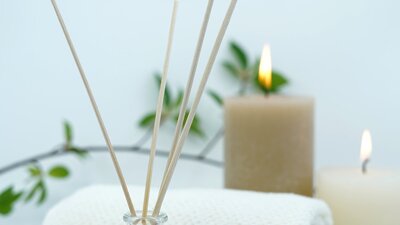 Reed diffuser, towel and lit candles against a white backdrop.