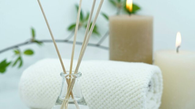 Reed diffuser, towel and lit candles against a white backdrop.