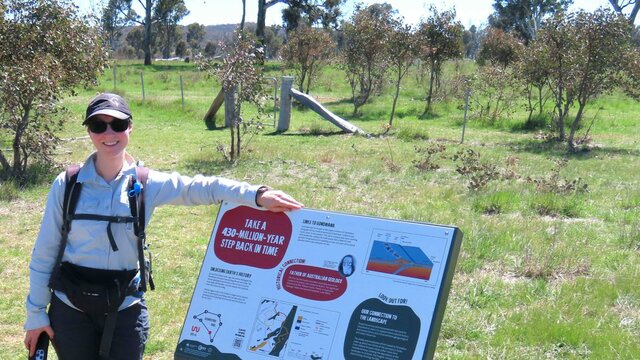 Stop 1 of the Mulligans Flat Geoheritage Trail revealing ancient secrets beneath Mulligans Flat Woman standing beside informative sign