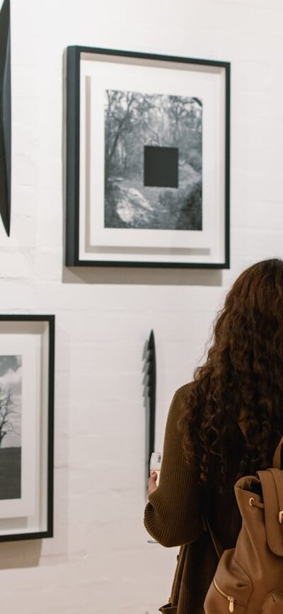 Two women are looking at framed photographs on the gallery wall