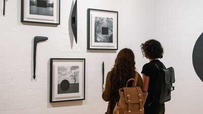 Two women are looking at framed photographs on the gallery wall