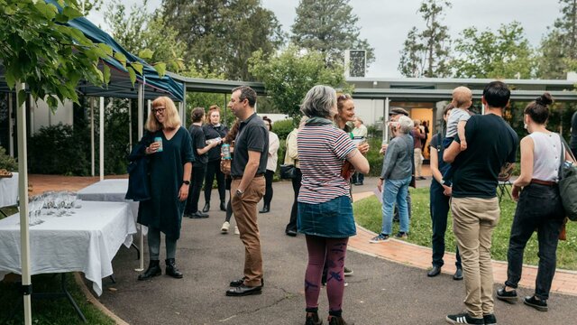 A summer outdoor exhibition opening A group of poeple stand outside eating nibbles and drinking champage
