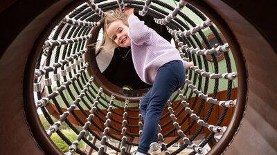 Young girl smiling at camera as she climbs through a net tunnel