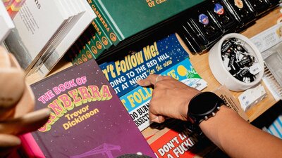 A close-up of a shopper’s hand browsing a selection of Canberra-themed books, stickers