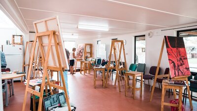 Several easels holding large canvases are set up in a large room.