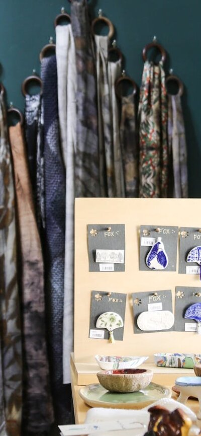 Scarves hang on a green wall behind a display table with jewellery.