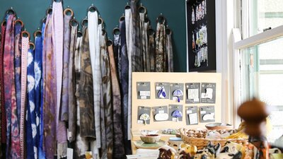 Scarves hang on a green wall behind a display table with jewellery.