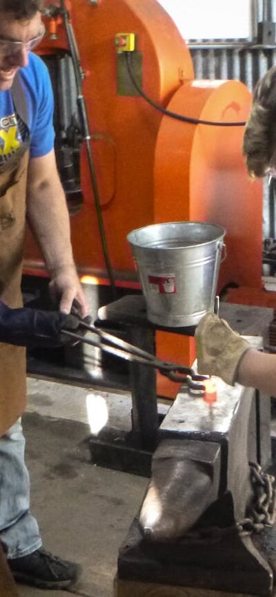 Man and children blacksmithing on an anvil