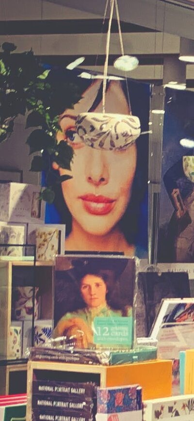 Posters of portraits from collection in the background with rows of boxed stationery