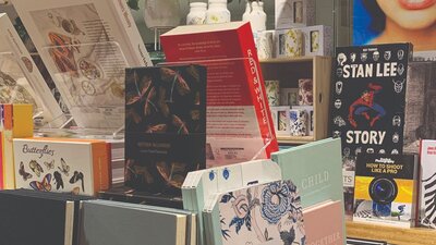 Boxed Stationary and books in foreground, ceramic tumblers and vases with botanical designs on raise