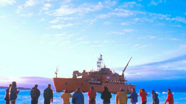 nla.obj-144071241 People in colorful winter gear stand on a vast icy plain, facing a large orange icebreaker ship.
