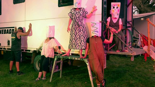 Tinnebago by Frank Lindner A photograph depicting five people wearing paper masks over their heads posing in front of a caravan