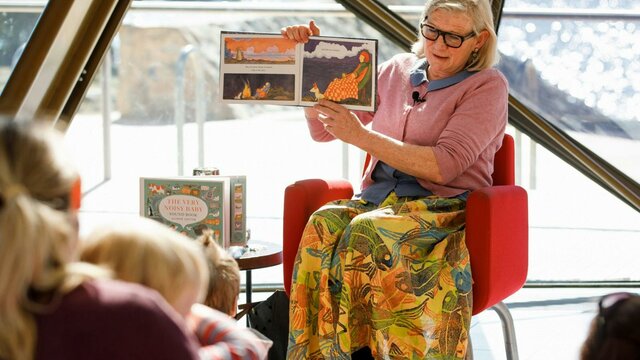 Alison Lester at the National Museum of Australia (detail). Woman sitting on a chair holding a book reading to a group of children.