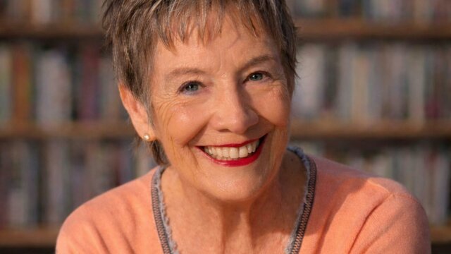 Catherine DeVrye A smiling, mature woman with short, gray hair, looking directly at the camera in front of a blurred