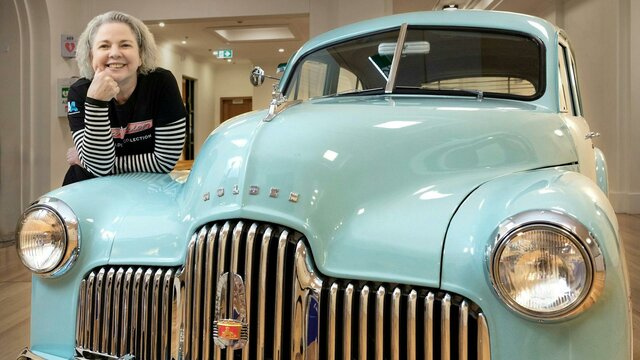 A woman poses on a vintage Holden car in an exhibition