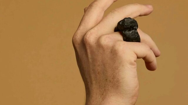 Matthew Freeman | Soma Erratics 1, 2025 A hand wears a large ring carved out of a dark material against a tan background