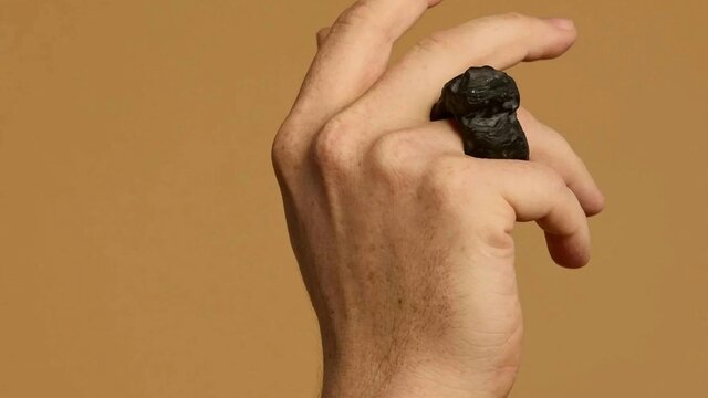 Matthew Freeman | Soma Erratics 1, 2025 A hand wears a large ring carved out of a dark material against a tan background