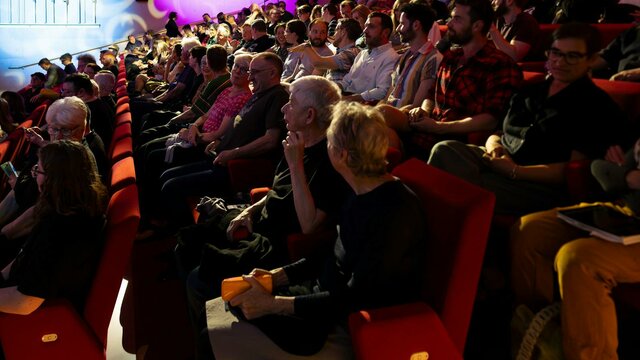 Don't Forget to Remember, 2024. National Gallery of Australia, Kamberri/Canberra. A photograph of a seated theatre audience talking with coloured lights in the background