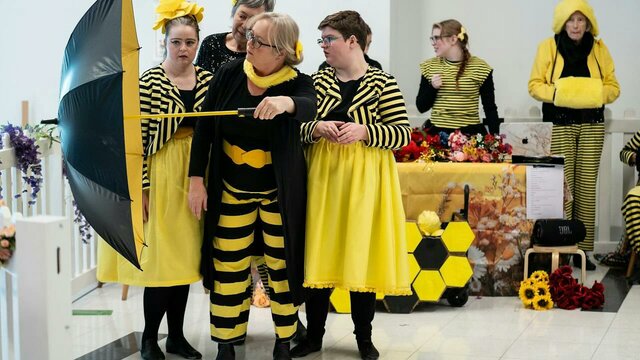 A group of dancers dressed in yellow and black reminiscent of bees perform with umbrella
